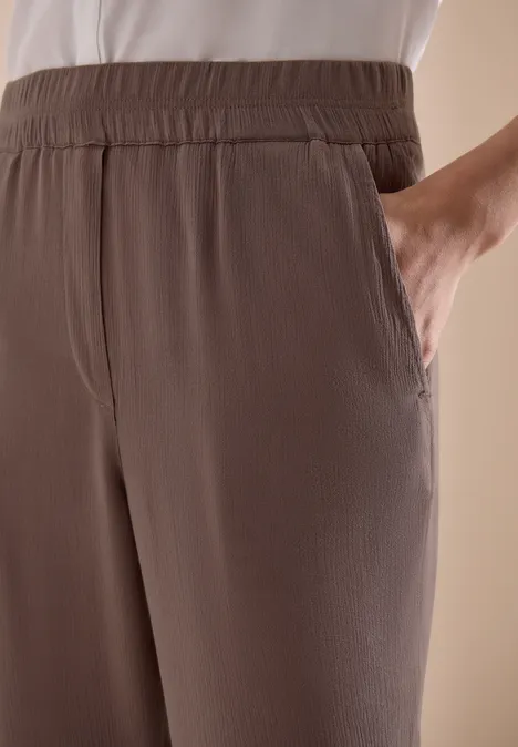 Bruine vrijetijdsbroek met elastische tailleband en zijzakken, hand in de zak gestoken.