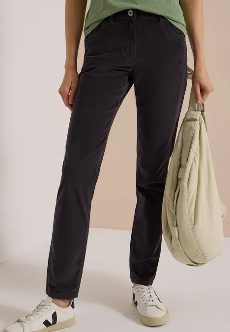 Personne en pantalon noir droit, baskets blanches et sac vert clair.