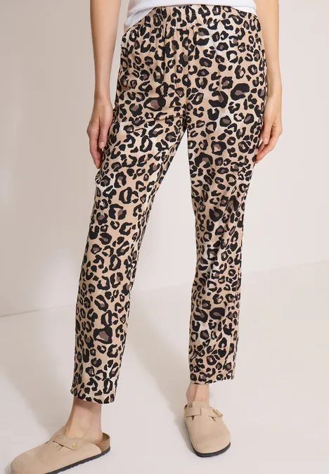 Beine in schmal geschnittenen, beige Leopardenmuster-Hosen und beigen Slippers.