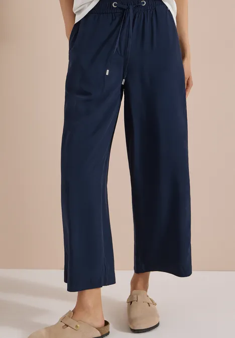 Dame trägt marineblaue, weite Hose mit Kordelzug und bequemen Slippern.