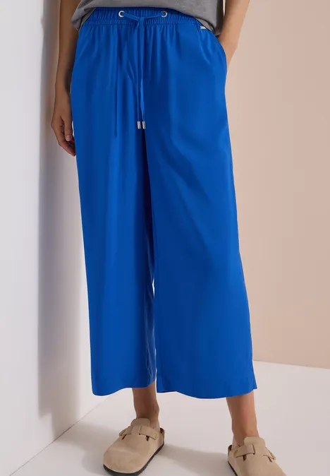 Knöchellange, weite blaue Hose mit Kordelzug und Taschen, dazu Sandalen