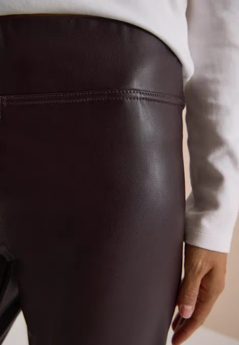 Strakke zwarte leren legging met wit bovenstuk, hand langs de dij.