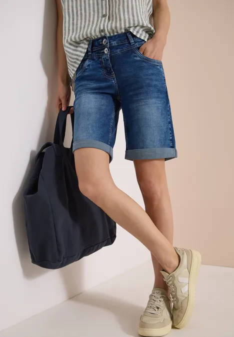 Person trägt knielange Jeans-Shorts, gestreiftes Top, Sneakers und eine dunkelblaue Tasche.