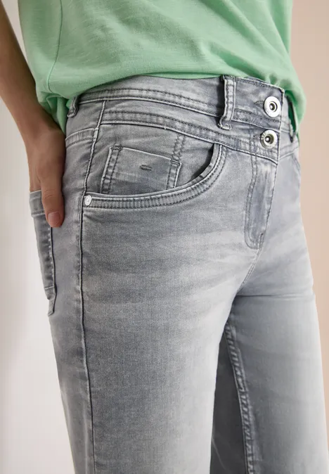 Close-up van iemand in lichtgrijze jeans en een groen shirt, hand in de zak.