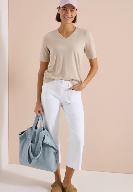Wide Leg Jeans mit Patch Pockets White Eine Frau in beigem T-Shirt, weißen Capri-Jeans und großem hellblauen Shopper vor hellem Hintergrund.