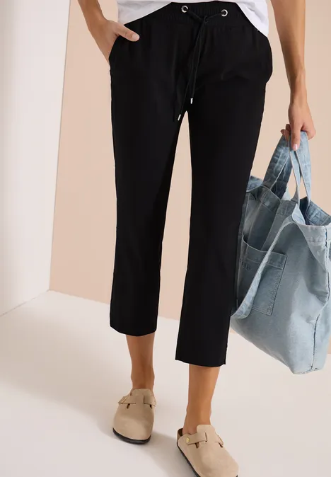 Strakke zwarte 7/8-broek met trekkoord, beige schoenen en grote denim tas.