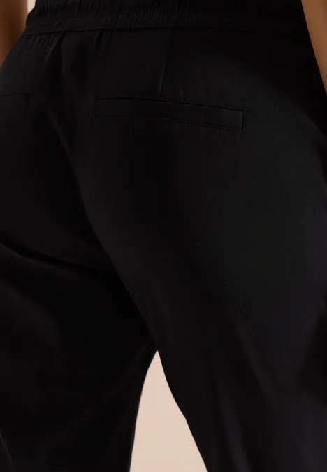 Close-up van een persoon in zwarte broek, zijdelingse heup- en beenpartij met zak.