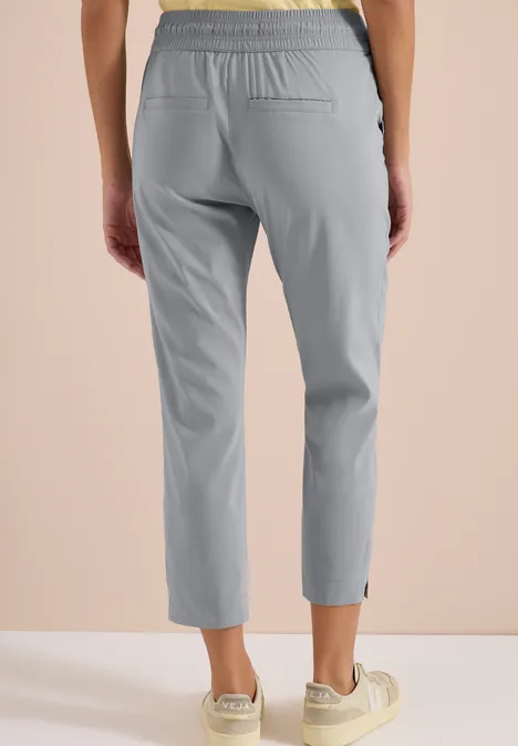 Grijs damesbroek tot op de enkel, met elastische taille, steekzakken en licht taps toelopende pijpen.