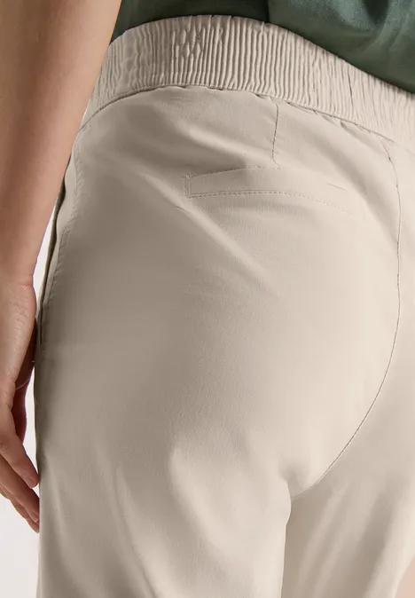 Close-up van een persoon in beige, hoog getailleerde broek met elastische tailleband.