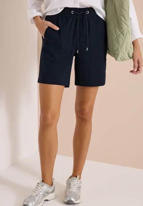 Straight Legs shorts in een Loose Fit universal blue Vrouw draagt marineblauwe short met koord, witte blouse, groene doorgestikte bodywarmer en zilveren sneakers.