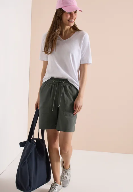 Straight Legs shorts in een Loose Fit clear khaki Jonge vrouw in wit T-shirt, kaki shorts, roze pet en sneakers, draagt een donkerblauwe tas.