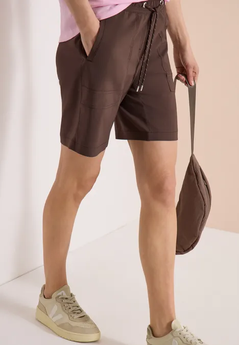 Straight Legs shorts in een Loose Fit brown cacao Persoon draagt bruine shorts, een roze top, beige sneakers en houdt een bijpassende bruine tas vast.