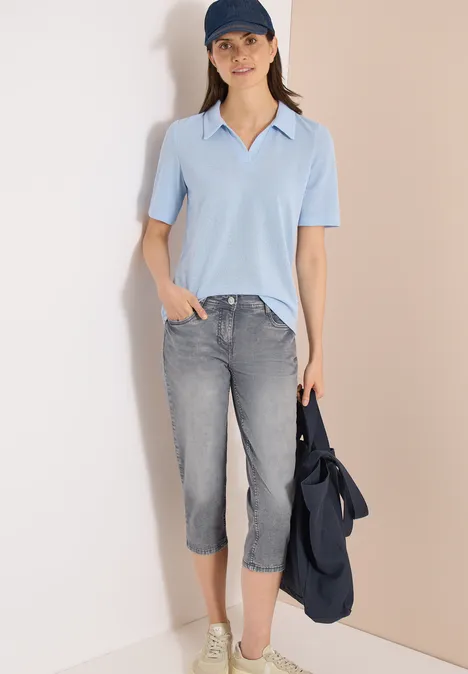 3/4 Slim Leg Jeans im Casual Fit mid grey used wash Frau trägt hellblauen Kurzarm-Pullover, graue Capri-Jeans und weiße Schuhe, hält eine blaue Jacke.