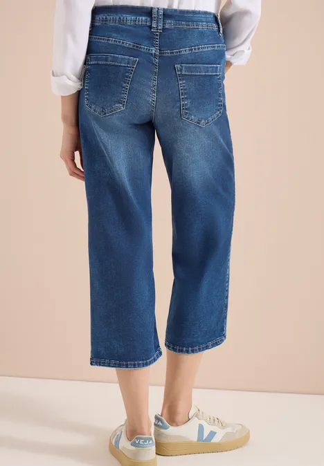 Rückansicht einer Person in weiten, knöchellangen Jeans-Culottes und weißen Sneakern.