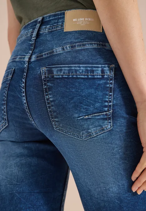 Een persoon van achteren draagt strakke, donkerblauwe jeans met zakken en een lichte used-look.
