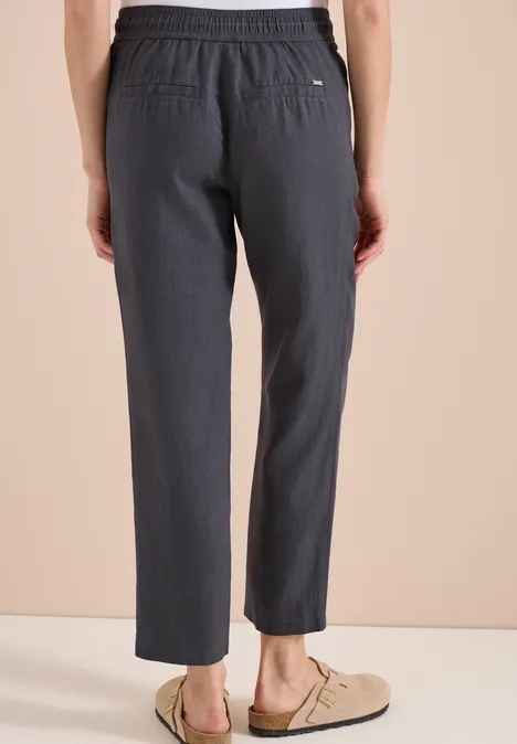 Rückansicht einer Person in grauen, locker sitzenden Hosen und beigen Slippern.