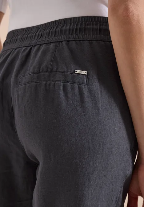 Hinterer Teil einer Person in dunkelgrauen Leinenhosen mit Gummibund und aufgesetzter Tasche samt kleinem Metalllogo