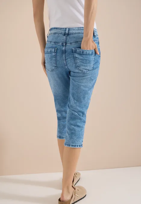 Person von hinten in hellblauer Capri-Jeans und beigen Espadrilles vor hellem Hintergrund.
