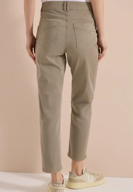 Vrouw van achteren in een kaki high-waist broek met opgestikte zakken en lichte sneakers.