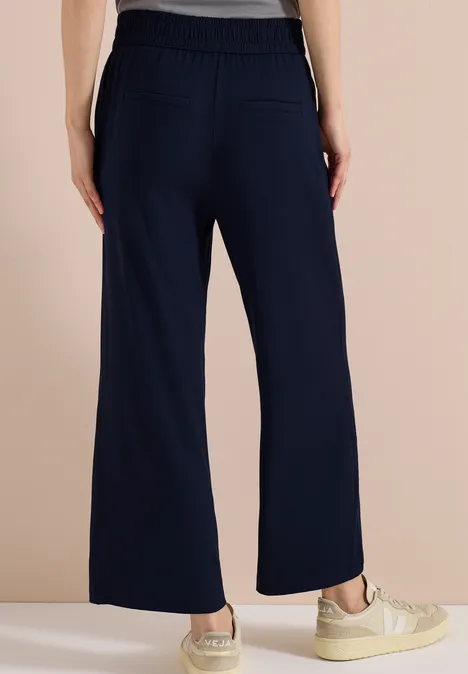 Rückansicht einer Person in dunkelblauen, weit geschnittenen Hosen mit elastischem Bund und Sneakern.