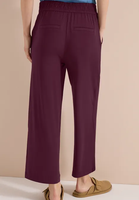 Rugaanzicht van een wijde pruimkleurige broek met elastische taille en twee achterzakken, gecombineerd met mocassins.