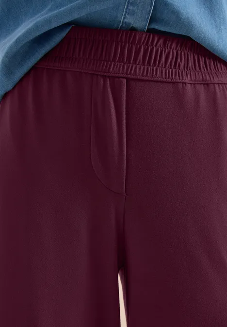 Bordeauxrode jerseybroek, losse pasvorm, elastische tailleband en zijzak.