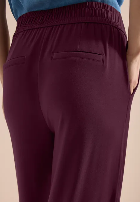 Achteraanzicht van persoon in bordeauxrode broek met elastische tailleband en paspelzakken.