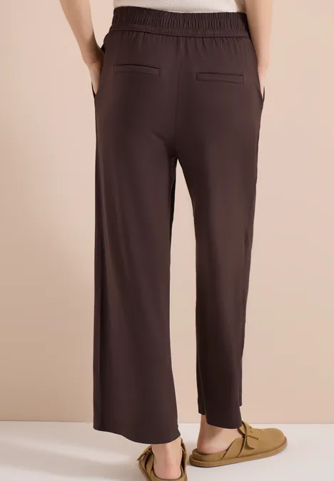 Femme de dos portant un pantalon marron foncé à taille élastique, coupe droite et poches passepoilées.