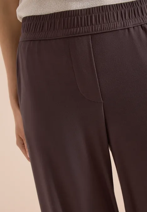 Gros plan sur un pantalon marron à taille élastique en tissu doux porté par une personne.