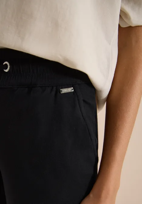 Nahaufnahme eines Oberkörpers in weißem T-Shirt und schwarzer elastischer Hose mit Tasche.