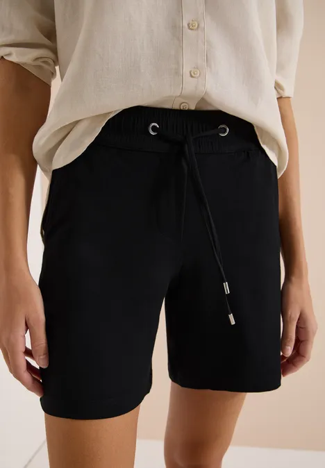 Schwarze, knielange Shorts mit Kordelzug, kombiniert mit lockerem, hellem Oberteil.