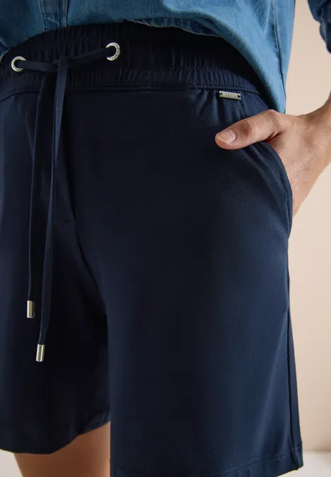 Nahaufnahme einer Person in dunkelblauen Jersey-Shorts mit Kordelzug und seitlicher Tasche.