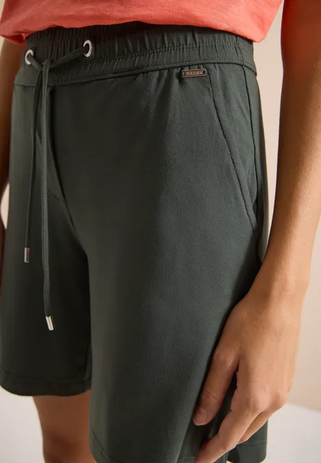 Nahaufnahme einer dunkelgrünen Shorts mit Kordelzug und Hand am Oberschenkel.