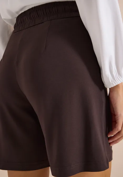 Wide Leg Shorts im Loose Fit brown cacao Rückansicht einer Person in schwarzen, lockeren Shorts und weißem Oberteil