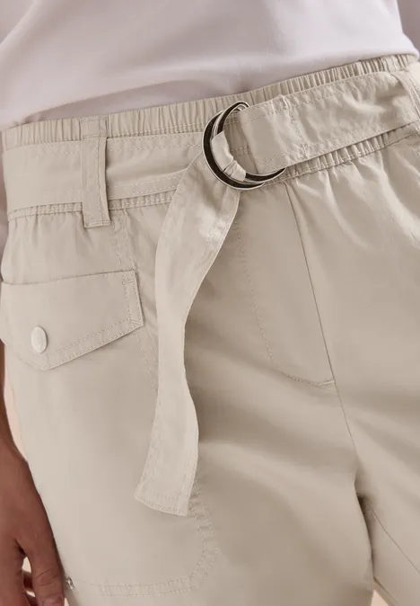Nahaufnahme einer hellbeigen Hose mit Stoffgürtel, D-Ring und Pattentasche.