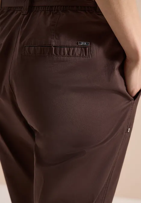 Nahaufnahme einer braunen Hose mit Hand in der seitlichen Tasche und kleinem Markenlabel.