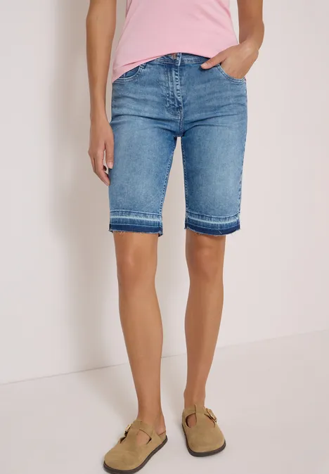 Frau trägt hellblaue Denim-Bermuda-Shorts und braune Sandalen, Oberteil in Rosa sichtbar.