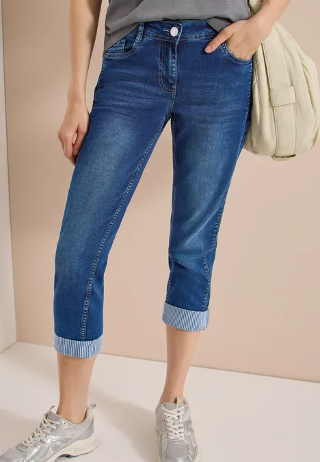 Mid Waist Straight Leg Jeans im Casual Fit mid blue wash Eine Person trägt dunkelblaue Capri-Jeans, hellgraue Sneaker und eine helle Umhängetasche.