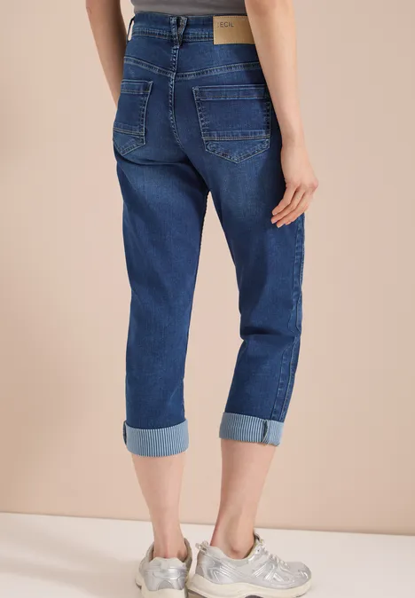 Mid Waist Straight Leg Jeans im Casual Fit mid blue wash Person von hinten im beigen Raum, trägt hochgekrempelte blaue Jeans und weiße Sneaker.