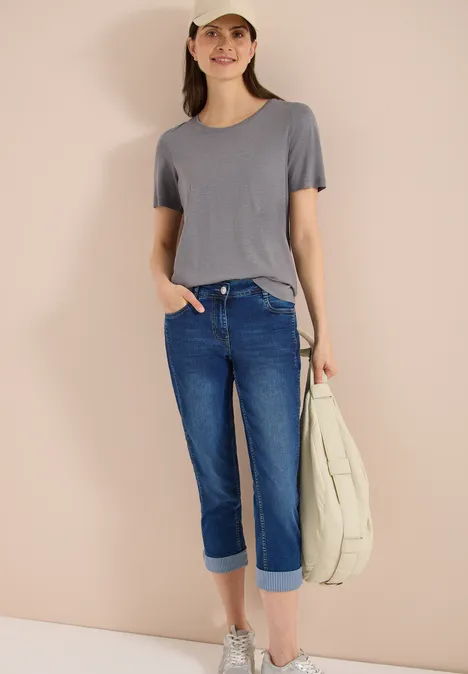 Mid Waist Straight Leg Jeans im Casual Fit mid blue wash Eine Person trägt ein graues T-Shirt, hochgekrempelte Jeans, glitzernde Slipper und hält eine helle Tasche.