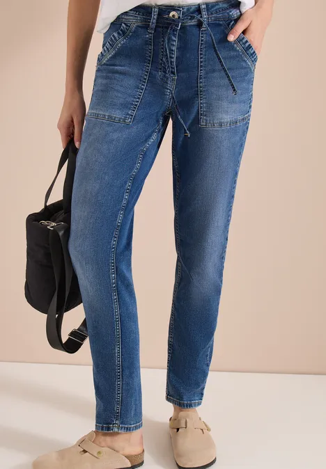 Blaue Jeans mit aufgesetzten Taschen und Gummizugbund, bequeme Schuhe und einen schwarzen Rucksack.