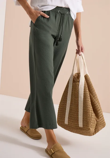 Vrouw in groene wijde broek, wit topje en grote strozak