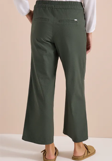 Achteraanzicht: model draagt donkergroene, wijde enkelbroek met elastische taille en casual loafers.