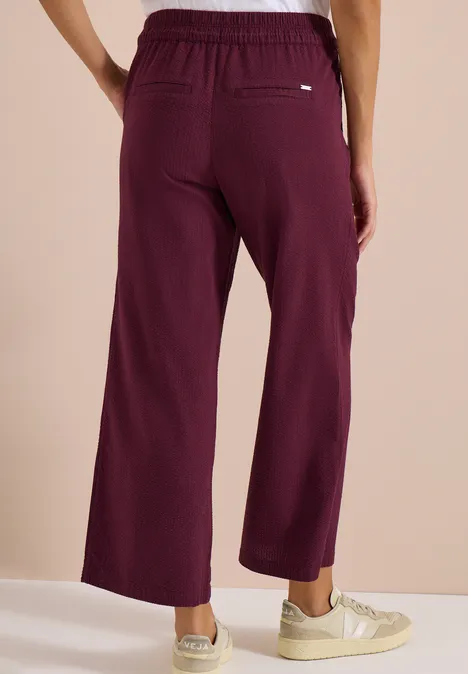 Modell trägt weite, dunkelrote Hose mit Gummibund, Rückansicht.