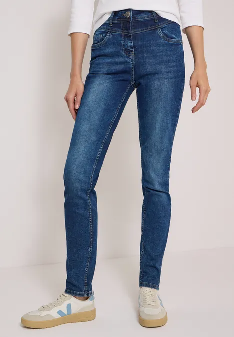 Person trägt blaue Skinny Jeans und weiße Sneakers, minimalistischer Hintergrund.
