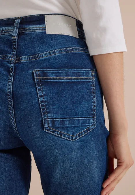 Rückansicht einer Person in blauen Jeans mit Gesäßtasche und weißem Oberteil, Hand an der Seite.