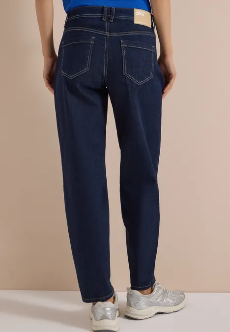 High Waist Barrel Leg Jeans im Loose Fit rinsed wash Eine Person steht von hinten, trägt dunkelblaue Jeans und helle Sneaker vor beigem Hintergrund.