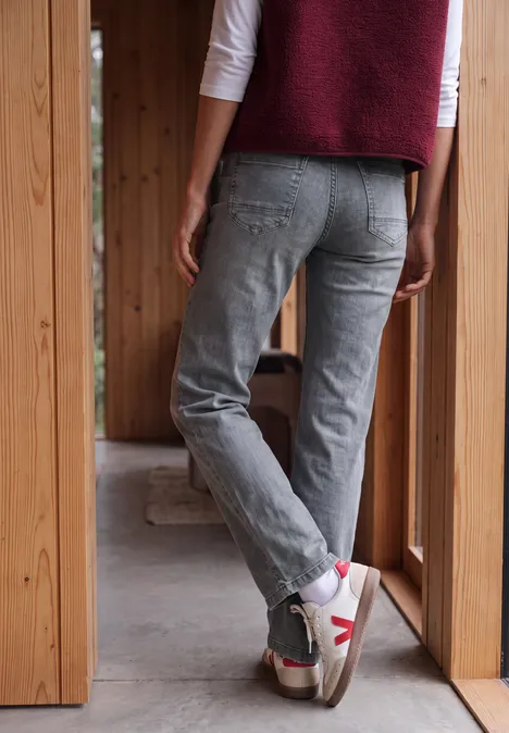 High Waist Wide Leg Jeans im Loose Fit light grey wash Person von hinten in grauen Jeans und weißen Sneakers steht in einer hölzernen Türöffnung.