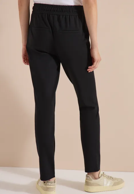 Schwarze Hose mit schmalem Schnitt und elastischem Bund, kombiniert mit beigen Sneakers.