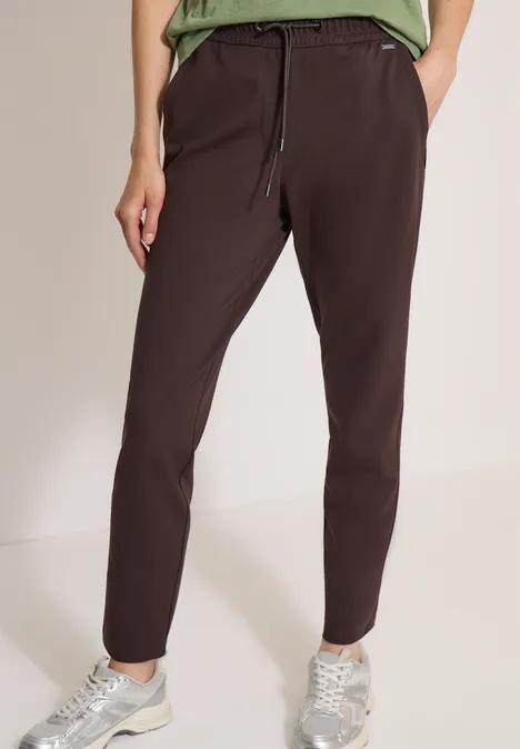 Dunkelbraune Damen-Hose mit elastischem Bund und Kordelzug, kombiniert mit Sneakers.
